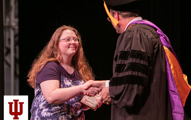 A man in a robe and mortarboard shakes hands with a woman