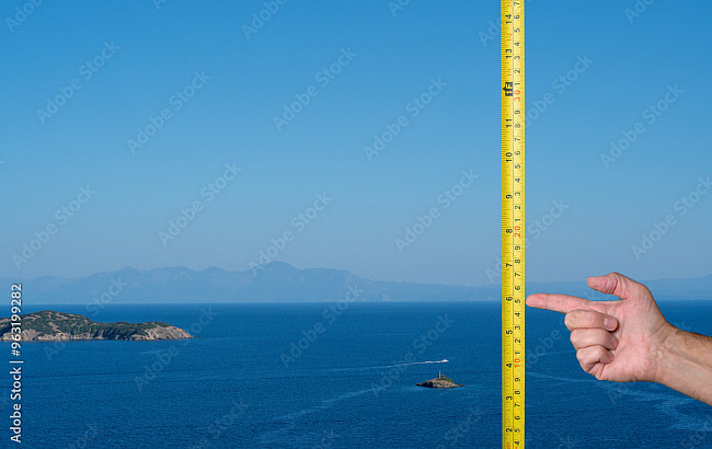 A hand points to a vertical tape measure in front of a blue ocean