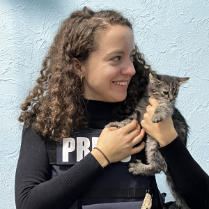 A woman in a vest labeled press holds a kitten.