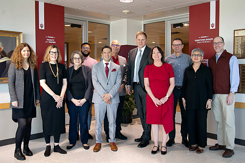 A large group of people stand in a hallway flanked by cream and crimson banners