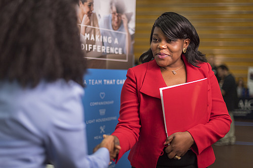 A woman in a red blazer shakes hands with an employer at a job fair