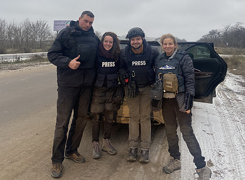 Four people in bulletproof vests stand on the side of a road in Ukraine.
