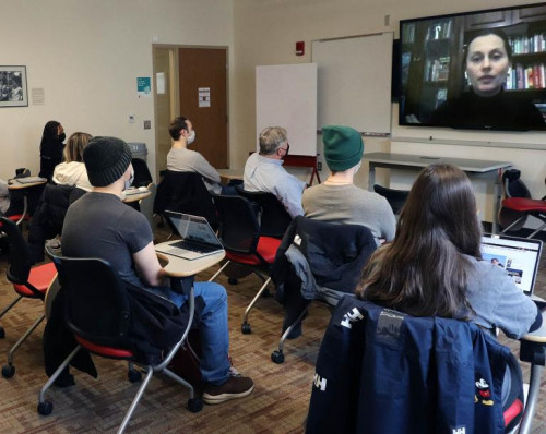 A woman speaks to a class via zoom on a television screen.
