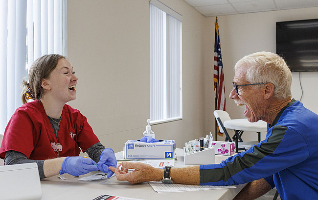 A man laughs as he speaks with a nurse who is preparing to test his cholesterol levels