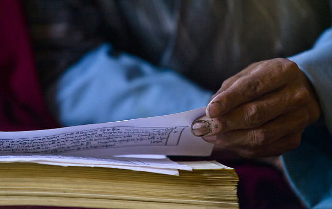 A hand turns a page with Sanskrit on it.