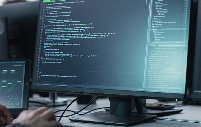 Hands type on a keyboard in front of multiple computer monitors
