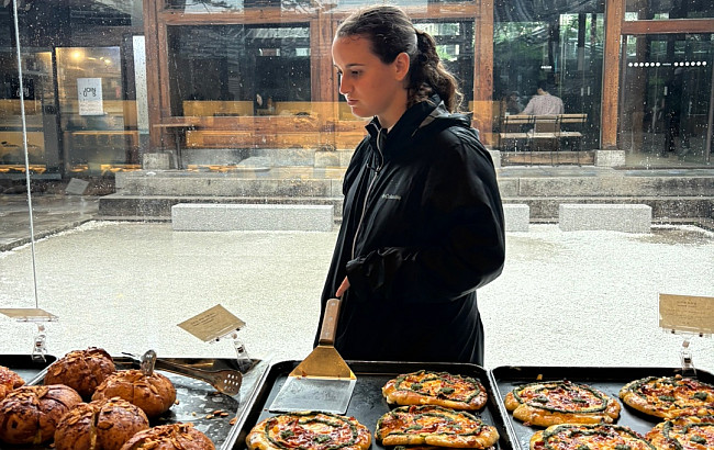 View from inside a South Korean bakery, looking out from the street, a woman stands in profile view, with a pagoda in the background