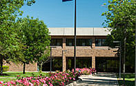 Façade and walkway leading up to Whitewater Hall, depicting flowerbeds, trees, and a flag pole with the U.S. and Indiana Flags