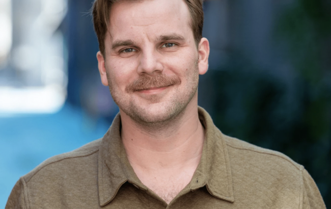 headshot of man in green shirt with mustache