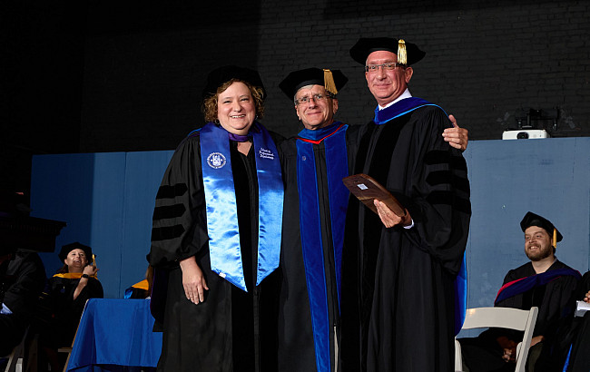 Woman and two men posing for a photo in graduation gear.