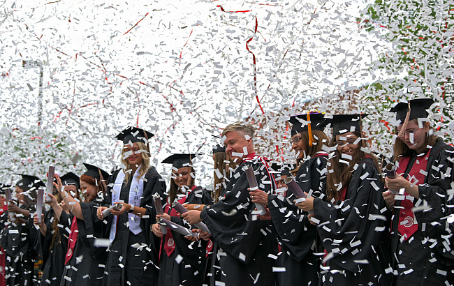 Graduates in graduation gear shoot off confetti poppers