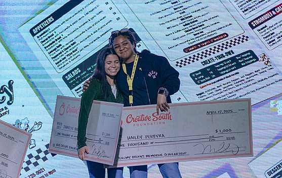 Two women holding large checks that represent the scholarships they won.