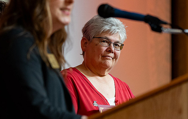 A lady in dark clothing stands at a microphone with another lady wearing red stands behind her.