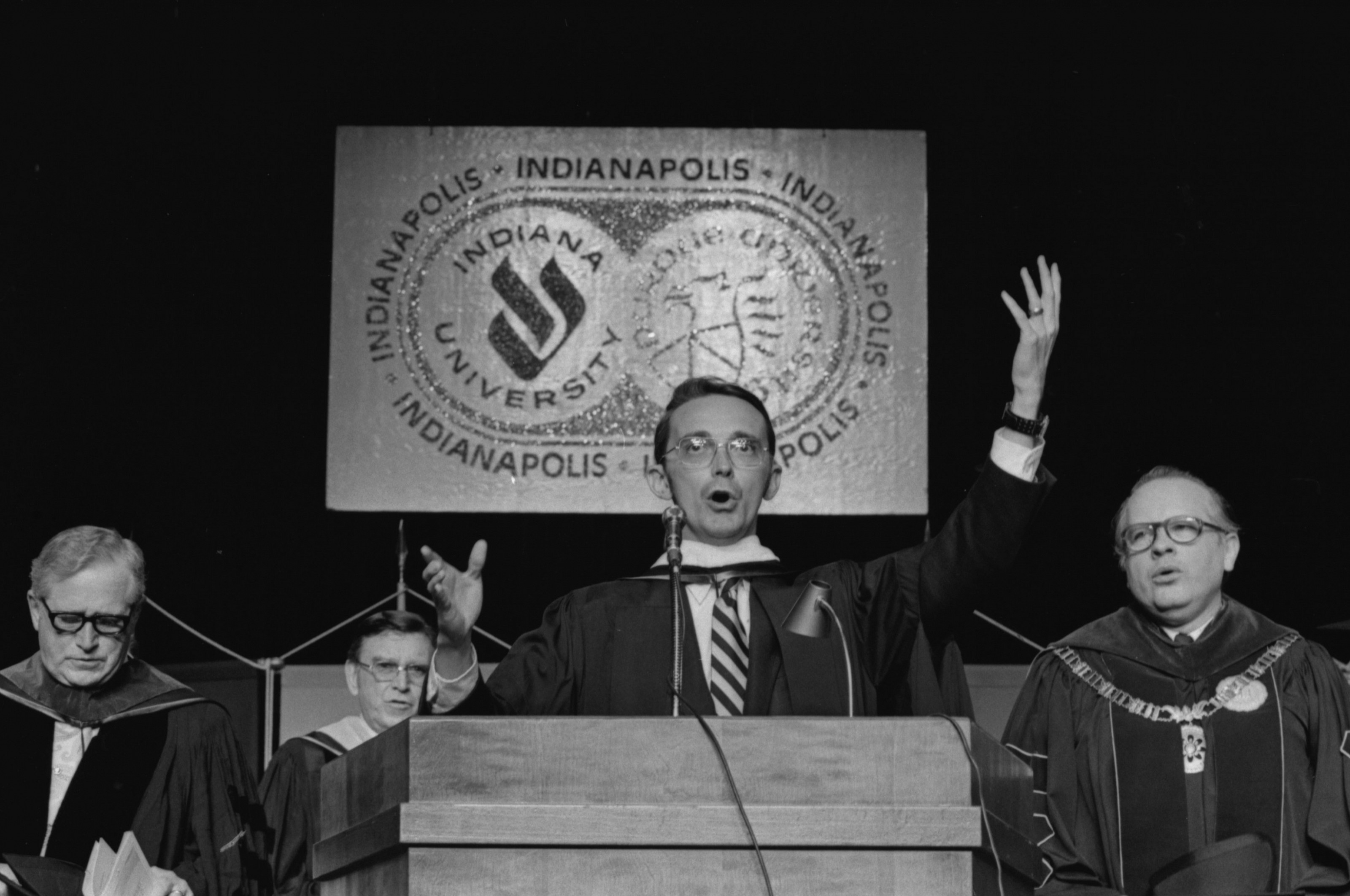 Black and white photo of a man singing on stage during a commencement ceremony