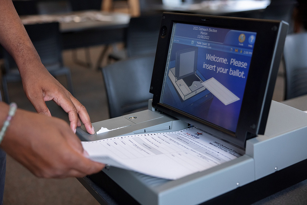 Close up of a hand inserting a ballot into a voting machine.