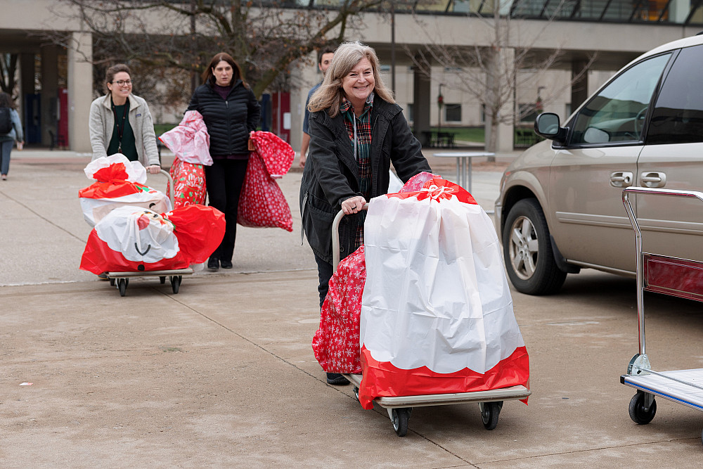 Two people push handcarts topped with wrapped holiday gifts.