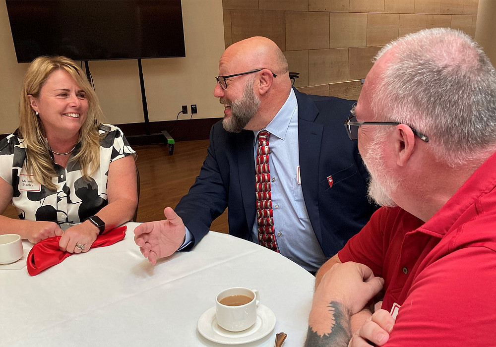 Faculty directors Melinda Stanley, left, and Michael Hutchins, right, talk with Mark Baer, interim assistant vice president of Online Aca...