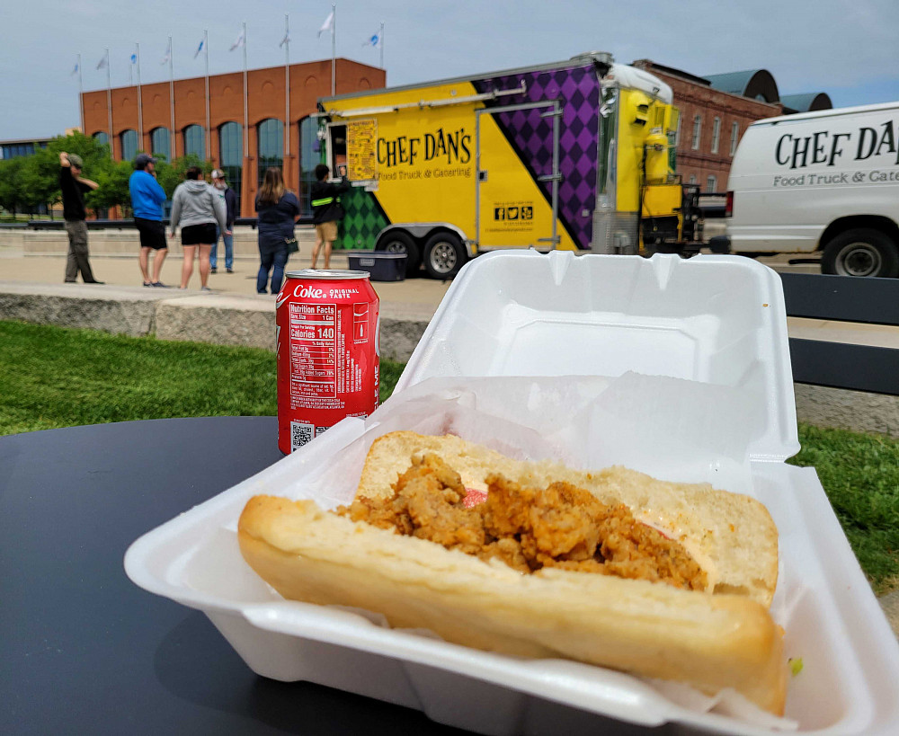 Sandwich and soda can in the foreground in front of a food truck.