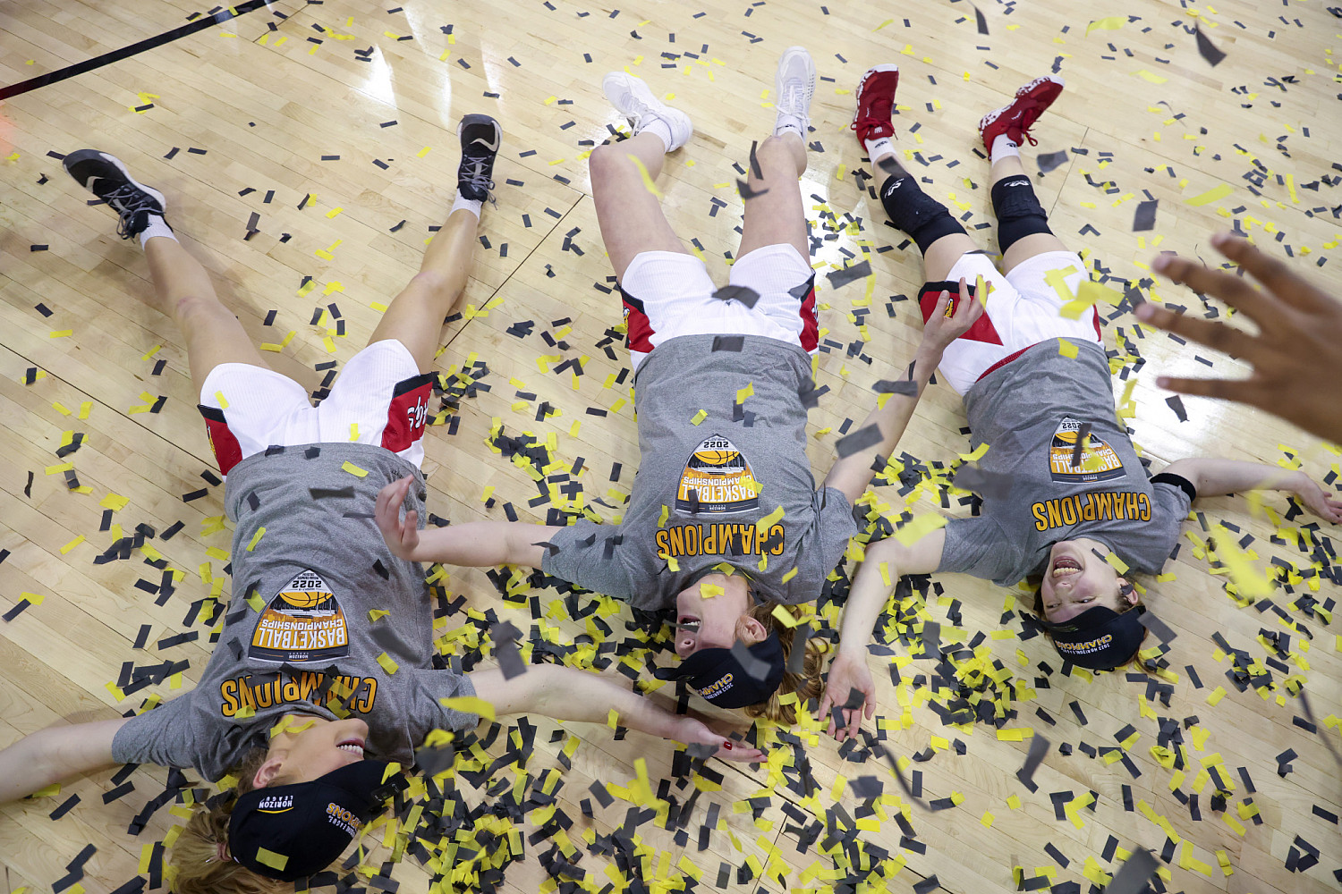 Three basketball players laying on the court in confetti