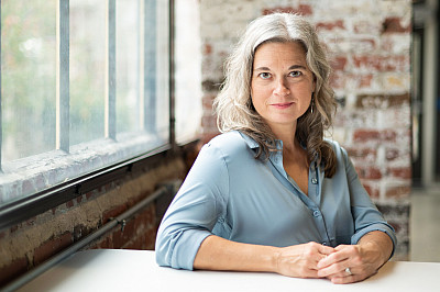 Brandi Smith sitting at a table next to a window and in front of a brick wall.